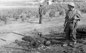 Soldados britânicos ao lado do corpo carbonizado de um paraquedista alemão durante a Batalha de Creta.